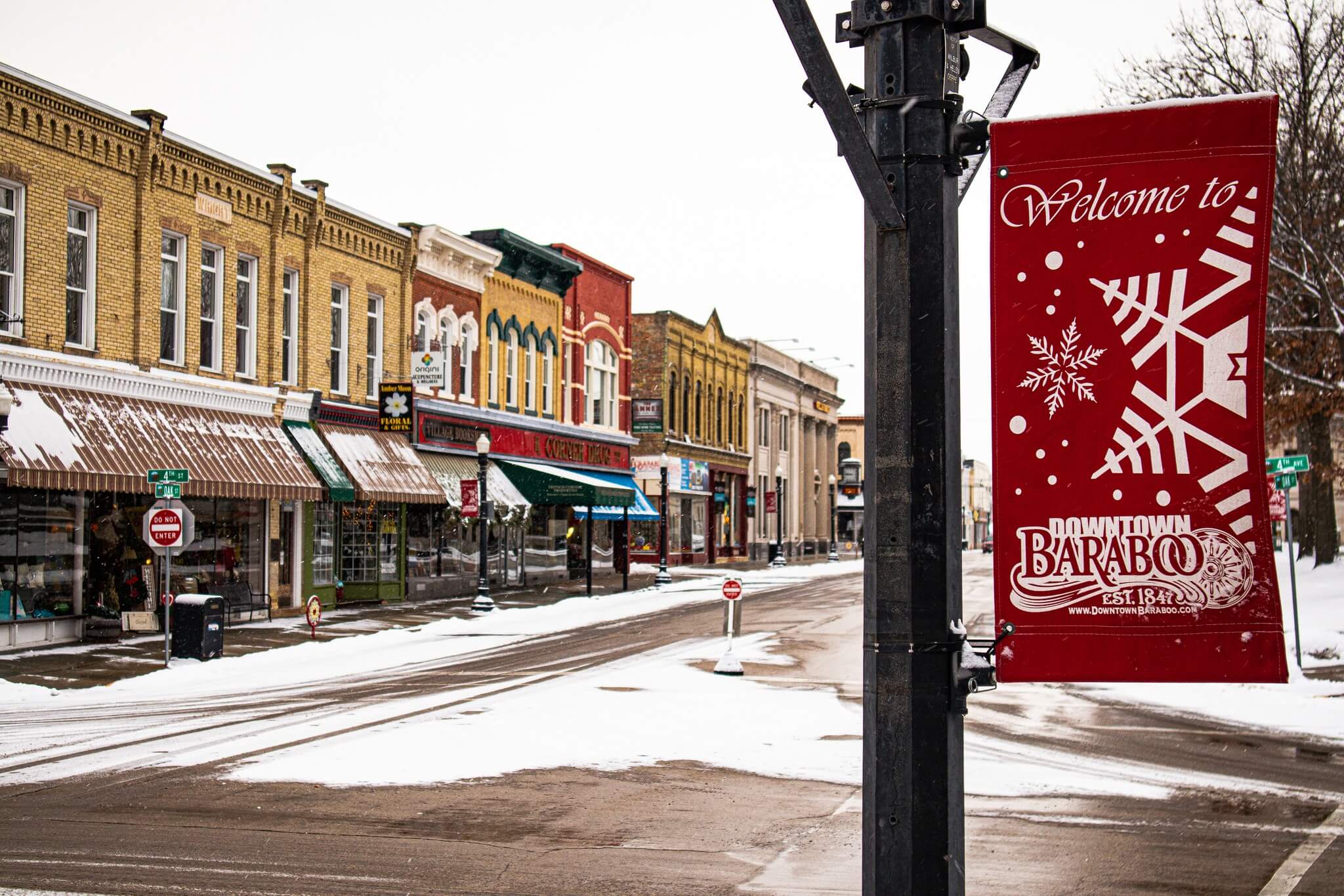 A snowy downtown street in Baraboo with a red Christmas banner on the light pole