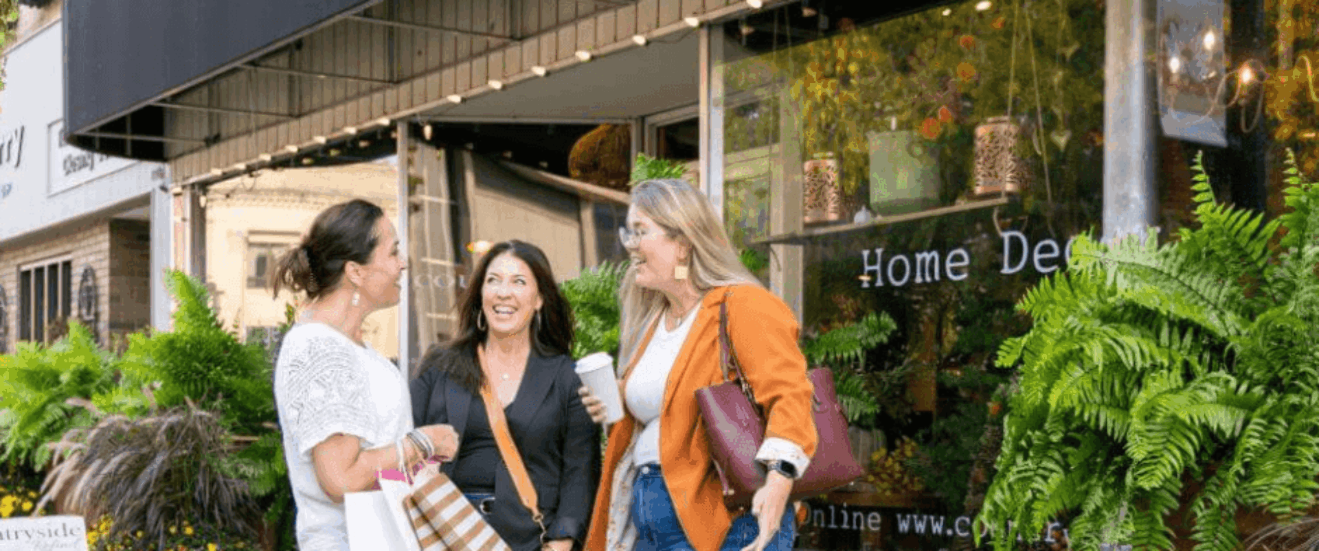Three women in downtown baraboo on the sidewalk with shopping bags smiling at each other