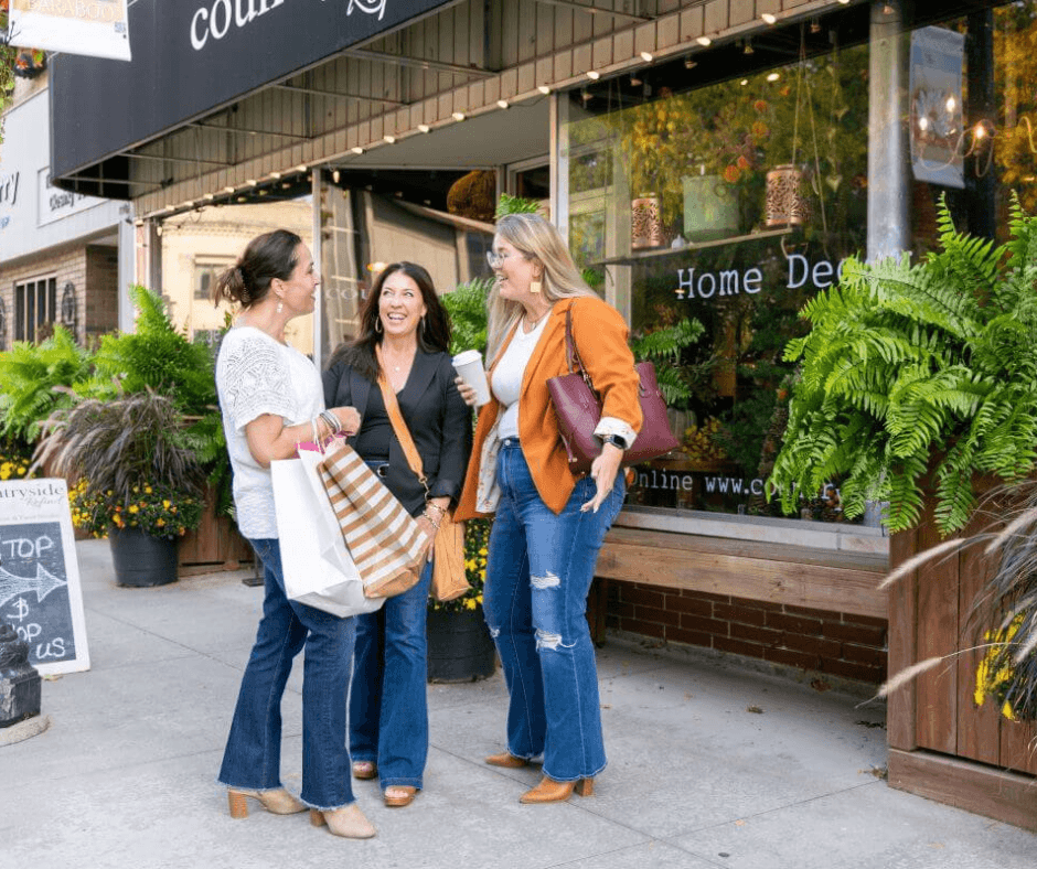 Three women in downtown baraboo on the sidewalk with shopping bags smiling at each other