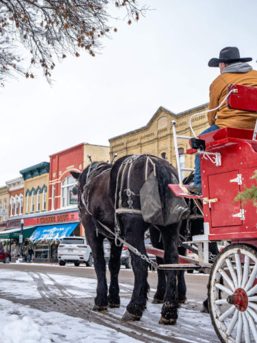 Two horses pulling a red carriage through Downtown Baraboo in the snow.