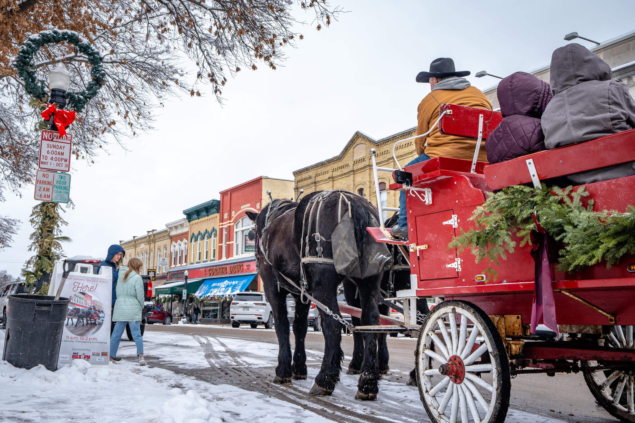 Two horses pulling a red carriage through Downtown Baraboo in the snow.