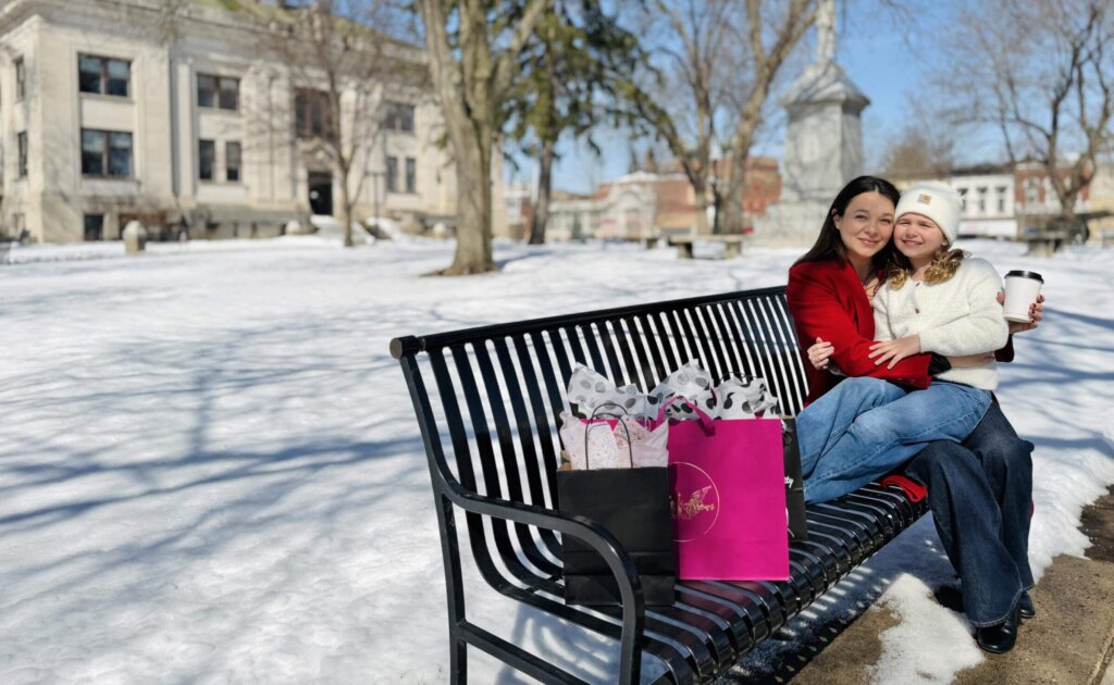A mom and daughter sitting on a bench with shopping bags in Downtown Baraboo on a snowy day.
