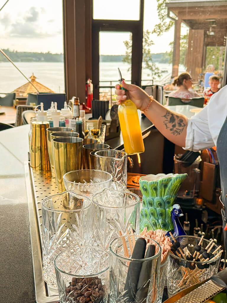 A bartender preparing a drink at the bar in Daylene's Supper Club, with a panoramic view of Lake Delton.