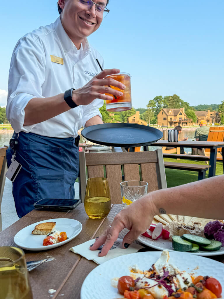 A waiter bringing an old fashioned drink to a group of ladies sitting outside at Daylene's Supper Club