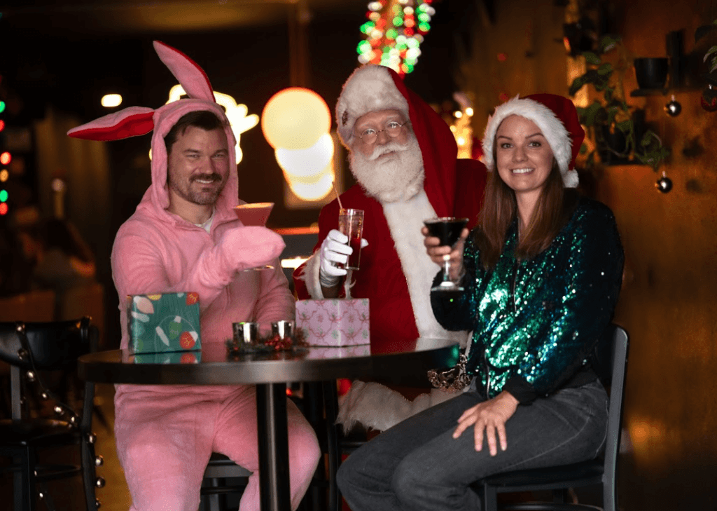Santa with two people in holiday attire drinking holiday beverages at a bar in downtown Baraboo