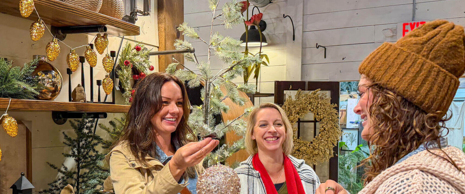 Three women shopping in a store for Christmas decorations. Looking at a large glittery white ornament and smiling.