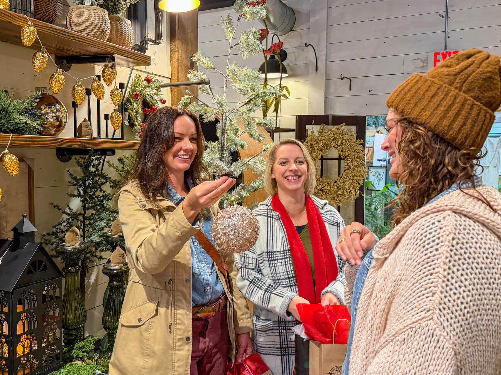 Three women shopping in a store for Christmas decorations. Looking at a large glittery white ornament and smiling.
